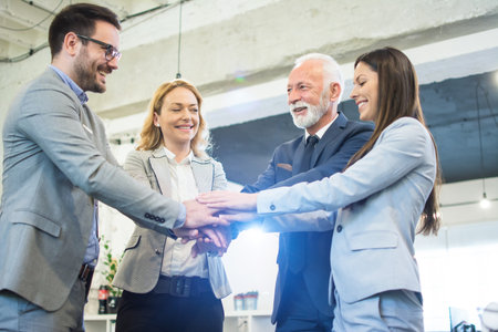 United coworkers standing with their hands together in modern office