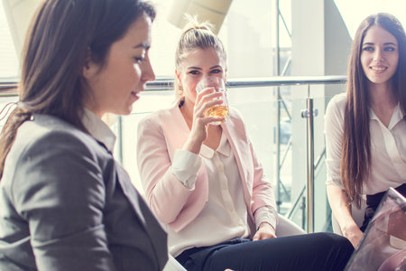 Portrait of a beautiful businesswoman having a drink with her colleagues sitting next to her in modern office building.の写真素材
