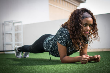 Beautiful African-American woman in sports clothing demonstrating plank exercise for abdominal strengthの写真素材