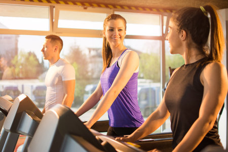Friends exercising together on treadmill in gym.