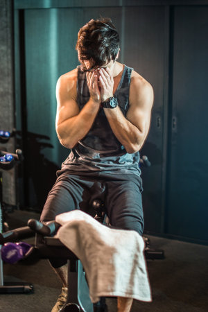 Muscular young man drying sweat from his face with hands after cycling workout in a gym.