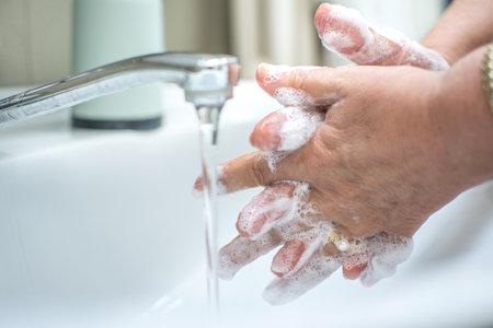 Young woman washing hands with soap over sink in bathroom, closeup.
