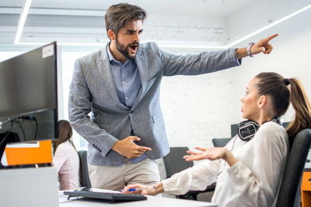 Young male business manager yelling at scared and stressed business woman at her workplace.