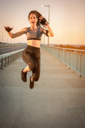 Athletic girl in sportswear jumping after successful training outdoors.