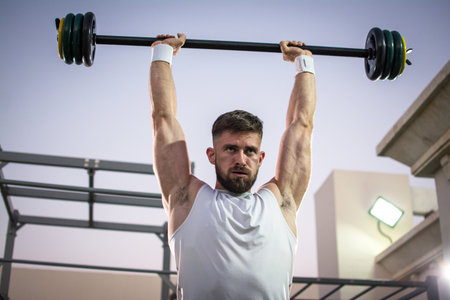Muscular young man lifting barbells in public gym
