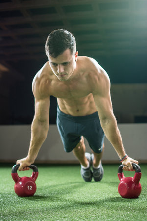 Concentrated muscular young man in plank position workout with kettle bells equipment in the gymの写真素材