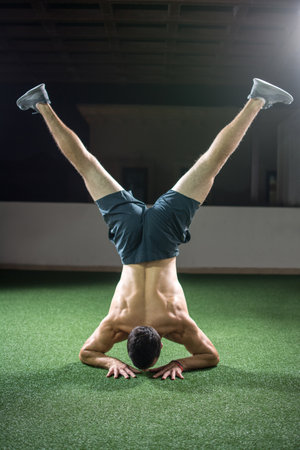 Back view of man standing on arms with raised legs