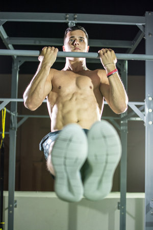 Young muscular man doing pull ups on horizontal bar outdoors