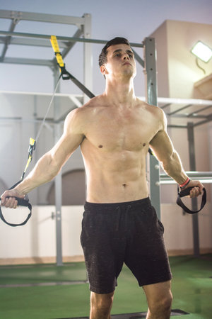 Muscular sportsman exercising with suspension straps at outdoor gymの写真素材