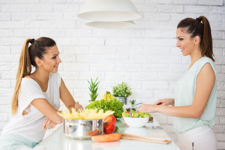 Happy young twin sisters preparing organic vegetables salad for lunch together in the kitchen.の写真素材