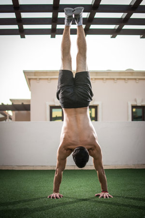 Back of handsome shirtless man doing handstand exercise outdoors
