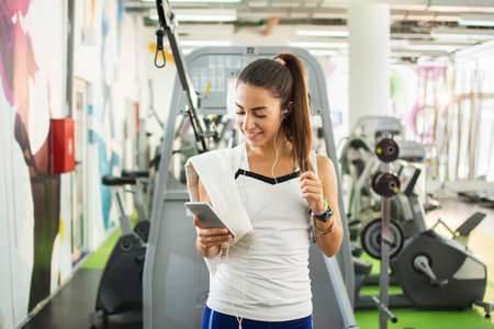Sportive girl using smartphone and listening to music in a gym