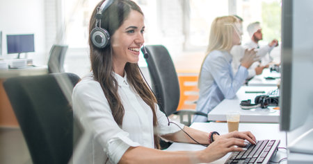 Portrait of beautiful smiling business woman with headset using computer in office.