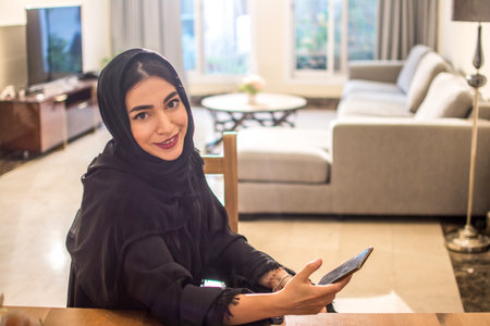 Portrait of smiling arab woman with smart phone in the living room at homeの写真素材
