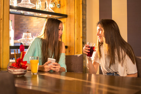Two high school girls drinking juices and talking in a cafe.