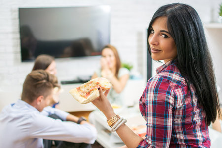 Young woman eating pizza with her friends at home.の写真素材