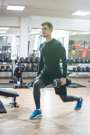 Muscular young man doing lunge exercise with weights in gymの写真素材