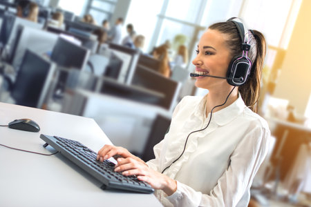 Friendly female helpline operator working on her workspace at large busy call center office