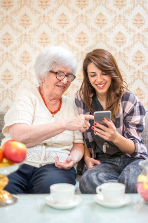 Grandmother showing something on smart phone to her granddaughter at home.の写真素材