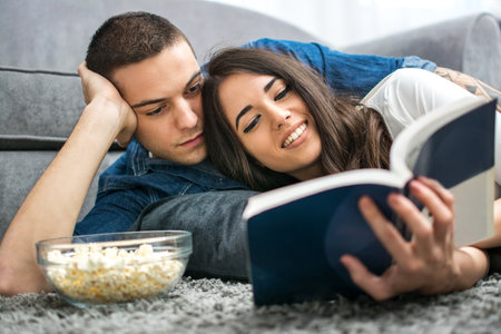 Young couple reading book together while lying on the floor.の写真素材