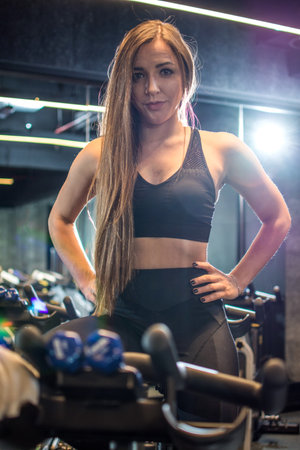 Portrait of beautiful slim sportswoman with long hair posing on exercise bike in gym