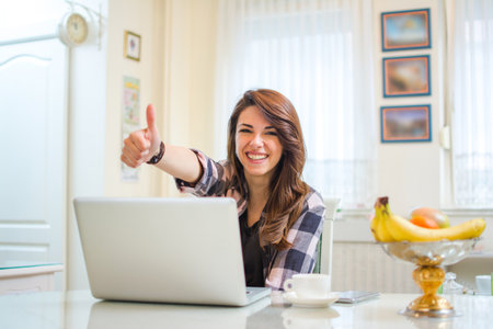 Confident entrepreneur working with laptop gesturing thumbs up looking at cameraの写真素材