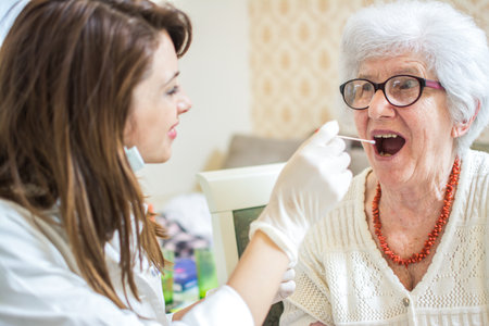 Young nurse or doctor checking the sore throat of a senior patient at home.