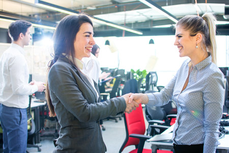 Two businesswomen shaking hands in modern office.の写真素材