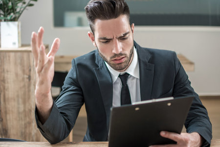Nervous businessman reading financial data over clipboard and hand gesturingの写真素材