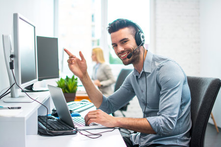 Attractive businessman with headset using laptop and computer in office.
