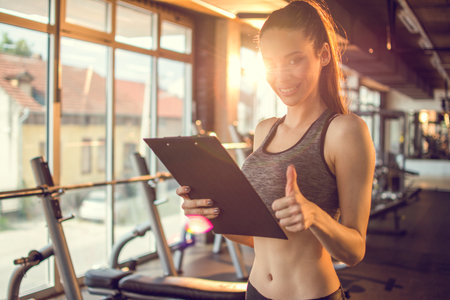Personal trainer with clipboard showing thumbs up in gym.の写真素材