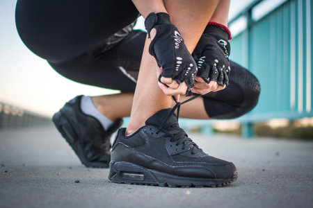 Close up view of womans hand in sports gloves tying shoe laces outdoors