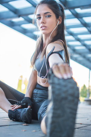 Beautiful sporty girl stretching outdoors. Young woman in sportswear touching toes while sitting on...