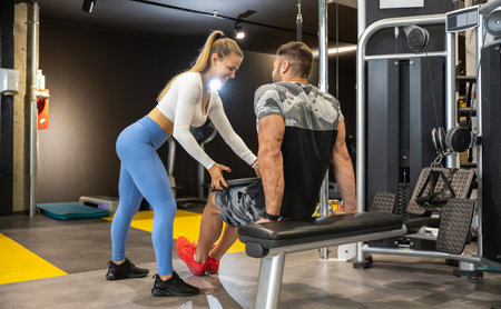 Muscular man exercising with heavy weight plate with assistance of girl at gym.