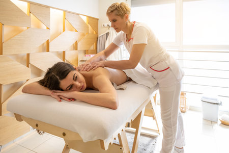 Female masseur massaging back of young client on massage table in spa center.の写真素材