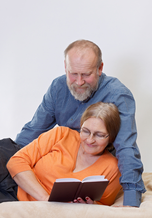 Happy couple lying in the bed and reading a bookの写真素材