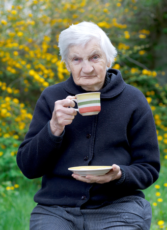 Elderly woman drinking her coffee in the gardenの写真素材