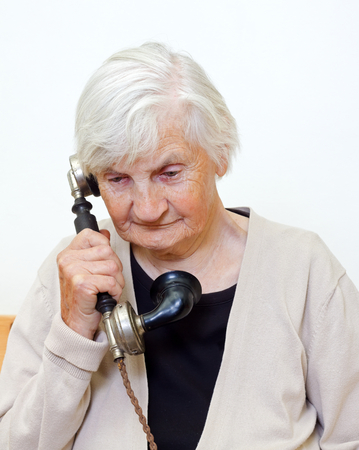 Elderly woman speaking on a retro telephoneの写真素材