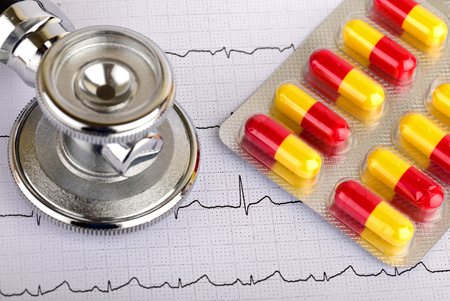 Electrocardiogram graph report with stethoscope and pills on itの写真素材