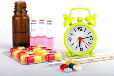 Picture of a green clock, colourful pills and capsulesの写真素材