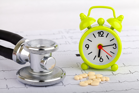 Electrocardiogram graph report with stethoscope and a clock on itの写真素材