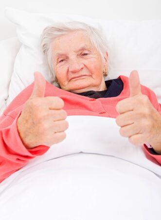 Happy senior woman resting in bed with thumbs upの写真素材