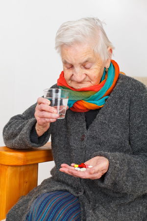 Picture of a senior woman sitting in her apartment and holding pillsの写真素材