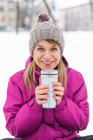 Picture of a beautiful young girl sitting in the snow, holding a cup of teaの写真素材