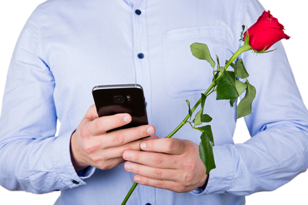 Close up picture of a young guy holding a red rose and texting his girlfriendの写真素材