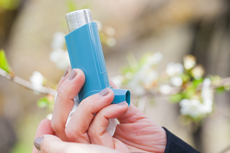 Close up picture of an asthma inhaler in a woman's hands outdoor during springtimeの写真素材