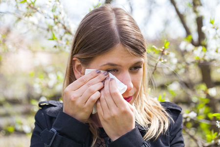 Young woman with allergy symptoms, sneezing, blowing her nose, springtimeの写真素材