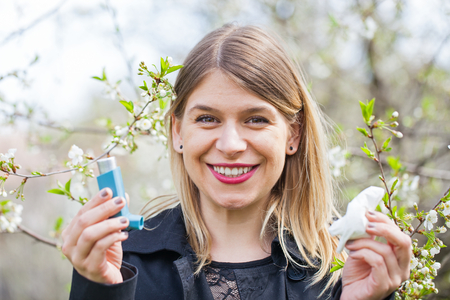 Picture of a young woman having pollen allergy, holding a bronchodilator outdoorの写真素材