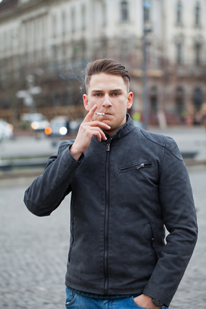 Picture of a handsome young man smoking a cigarette in the city, outdoorの写真素材