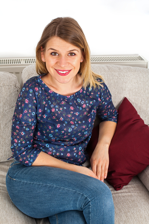 Picture of a smiling young woman sitting on the couch at home, indoorの写真素材